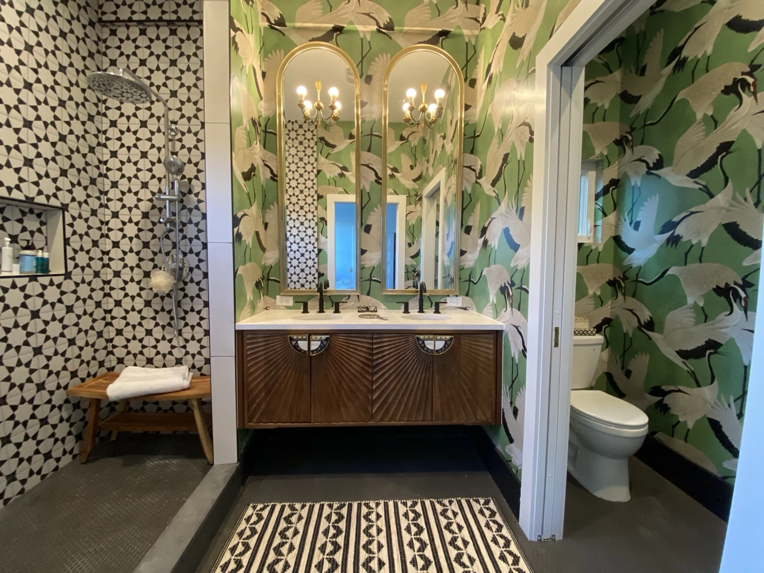 Bathroom with green crane wallpaper, twin gold mirrors and a geometric tiled shower