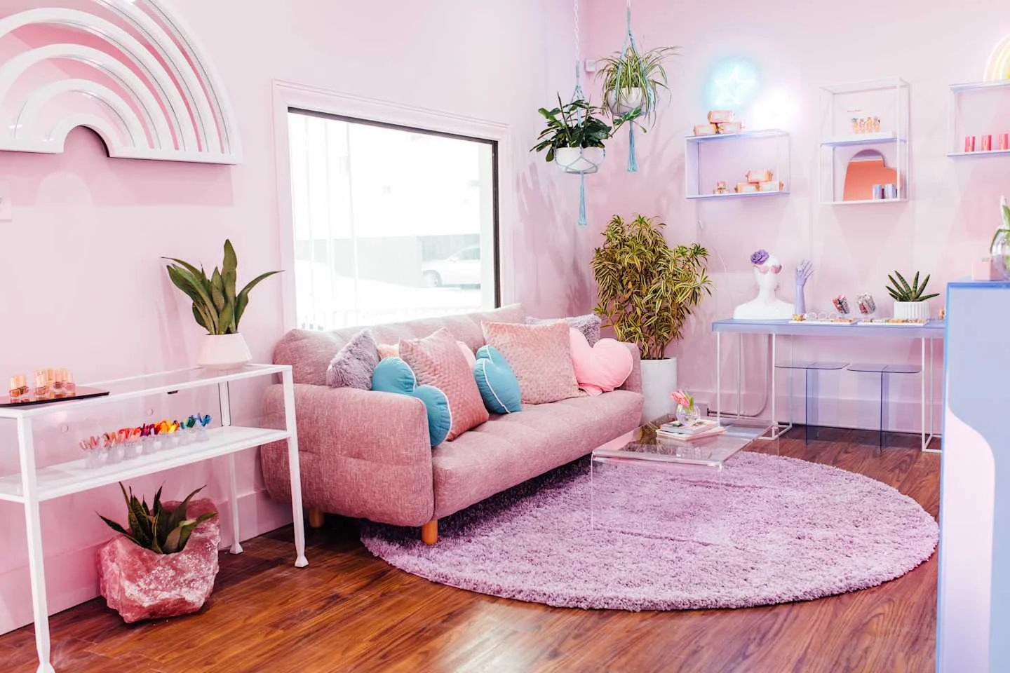 Pink salon lounge with a sofa, lilac rug, rainbow wall art and plants — Cute Nail Studio, East Austin, Texas