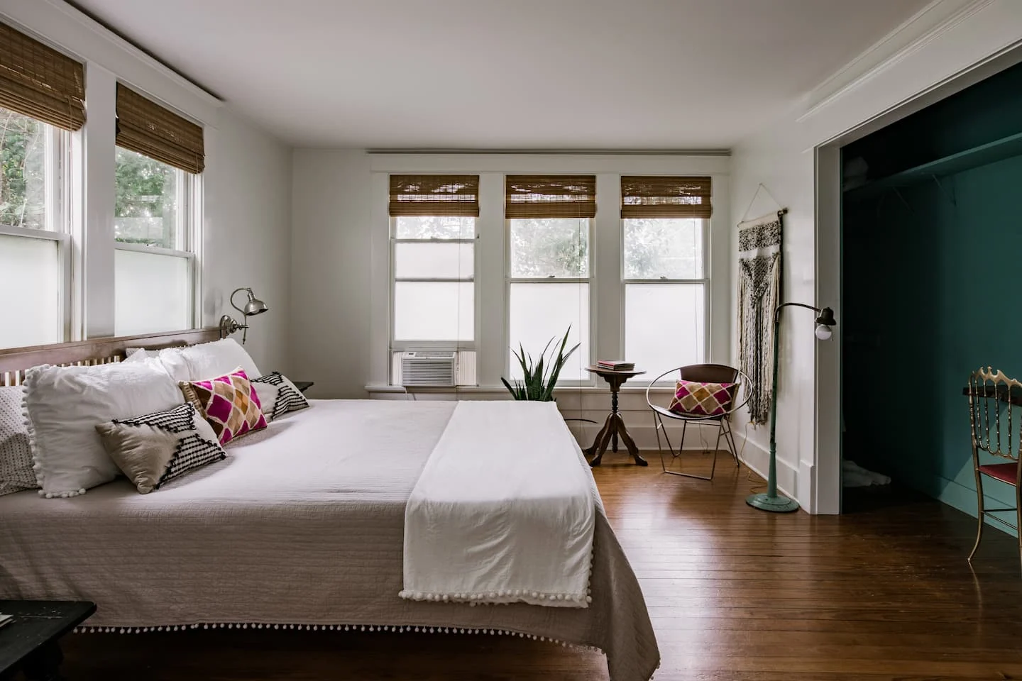 Airy bedroom with wood floors, white bedding and a dark green doorway — Navasota, Austin, Texas