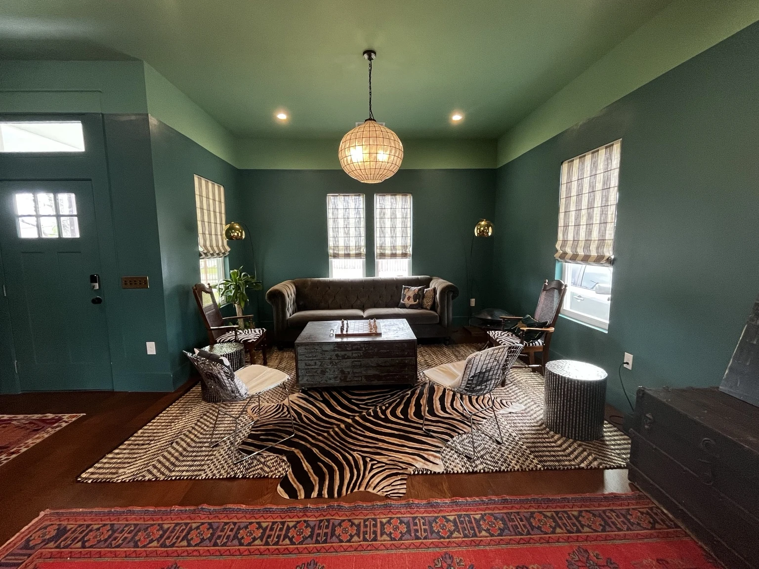 Teal living room with vintage seating, layered patterned rugs and a globe pendant