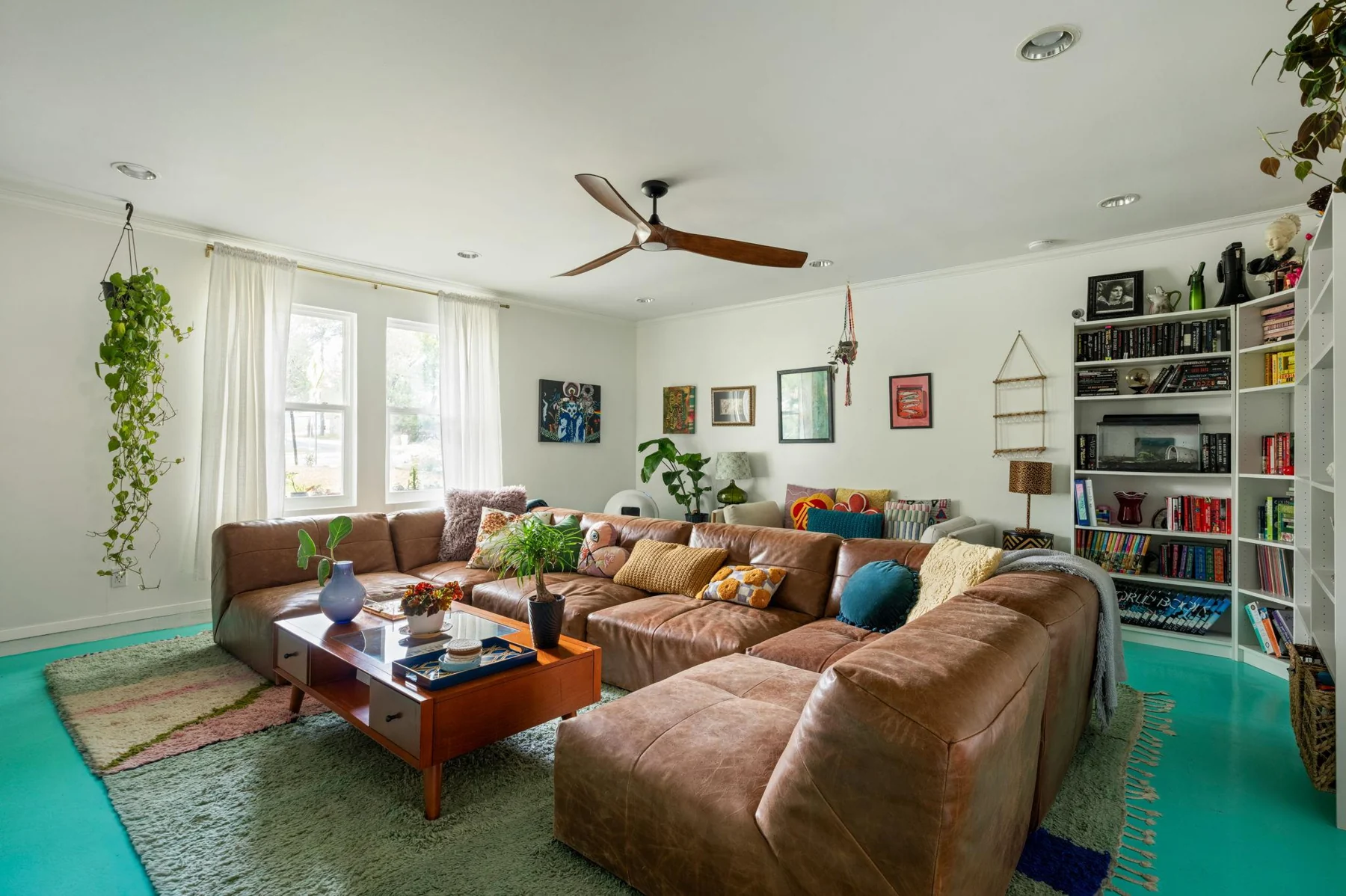 Living room with turquoise floor, a brown sectional and bookshelves — Woodhue, South Austin, Texas